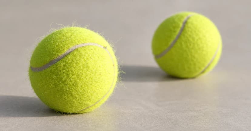 Two yellow-green tennis balls with pale curved seams rest on a neutral surface.