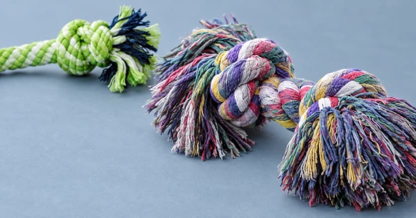 A multicolored rope knot with attached tassels and a green and navy braided section on a blue-gray tabletop.