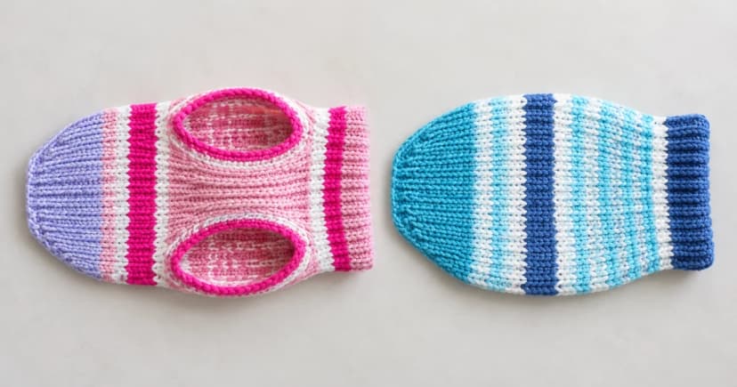 Two unworn striped knitted dog garments laid separately on a pale tabletop.