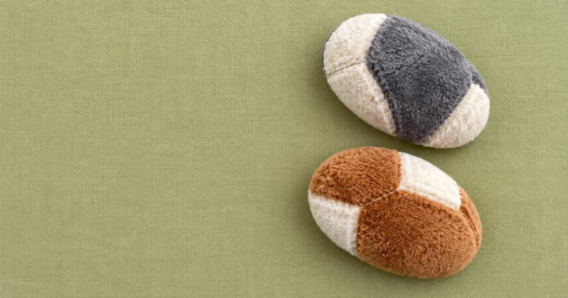 Two reconstructed oval brown-and-cream and gray-and-cream fabric forms resting apart on a pale-olive textile surface, viewed from above.