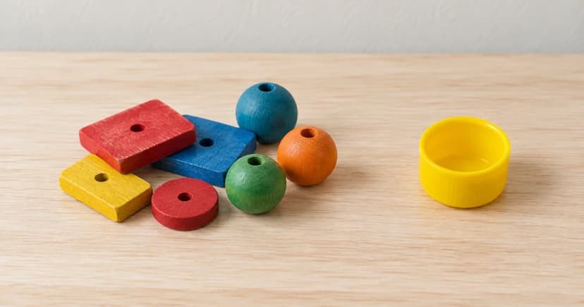 Separate colored toy pieces and a yellow cup-like piece on a wooden surface; edited bird-toy care illustration.