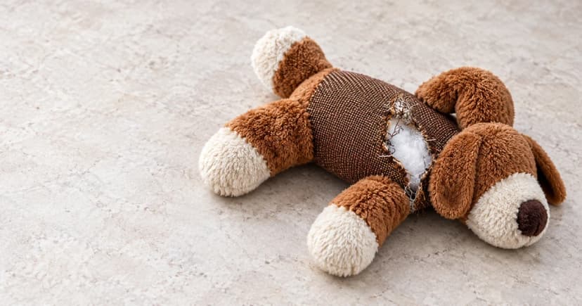 Reconstructed withdrawn brown-and-cream fabric toy with an open seam and exposed white filling on a pale surface, away from animals.