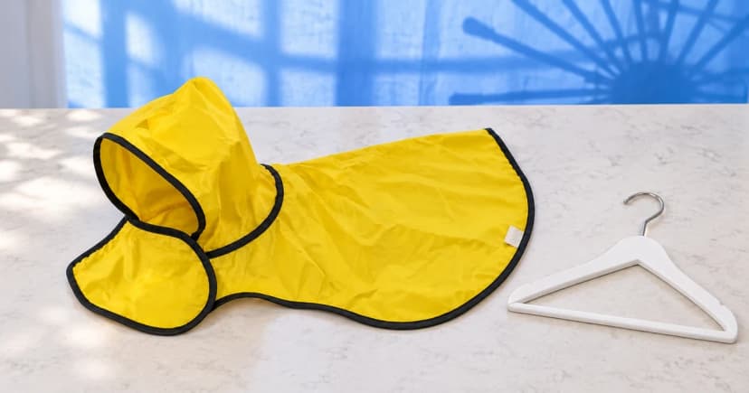 A complete yellow hooded dog raincoat laid flat beside a hanger, with a small care-label tab visible