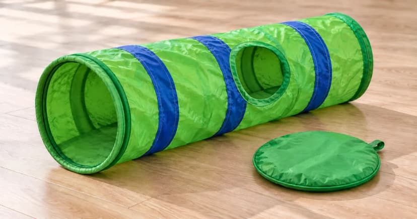 An empty green-and-blue fabric cat tunnel lies fully extended beside a separate storage pouch.