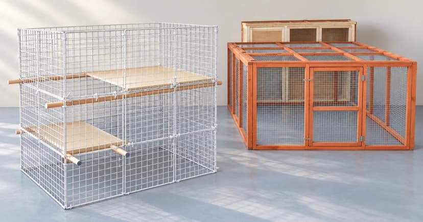 Separate white wire-grid and wood-framed mesh enclosure structures on a neutral floor.