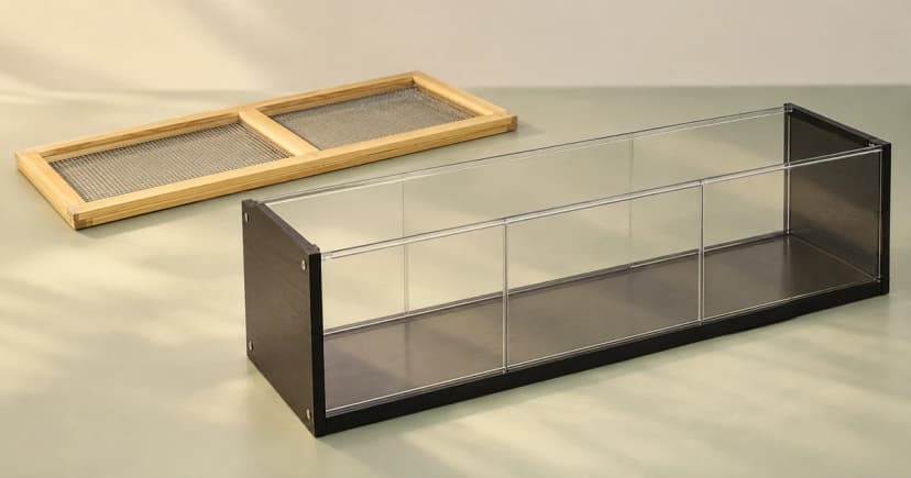 A generic empty clear-panel habitat shell beside a separate wooden mesh cover.