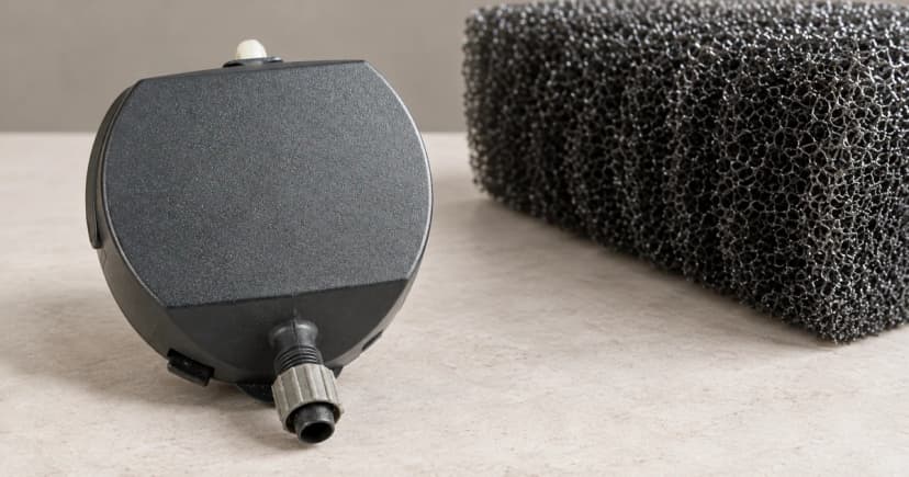 A separate dark aquarium pump casing and partial coarse foam block on a pale tabletop.