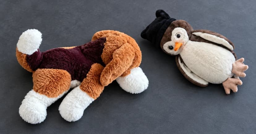 Brown and cream soft toy beside a separate penguin-shaped plush object on a slate tabletop.