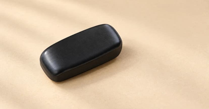 A single dark closed tracker case resting diagonally on a pale sand tabletop.