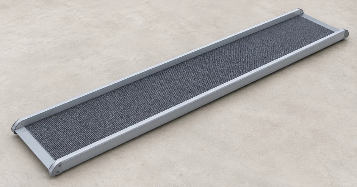 A long gray pet ramp lies flat on a plain floor, with both ends and raised side edges visible.